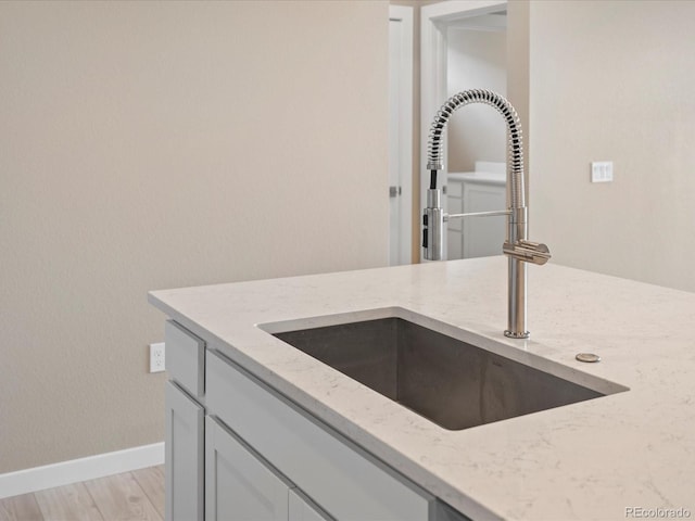 kitchen featuring gray cabinetry, light stone counters, light wood-type flooring, and sink