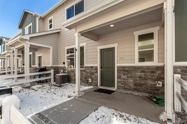 snow covered property entrance featuring stone siding, central AC, and fence