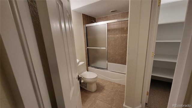 full bathroom featuring toilet, tile patterned flooring, a spacious closet, and bath / shower combo with glass door