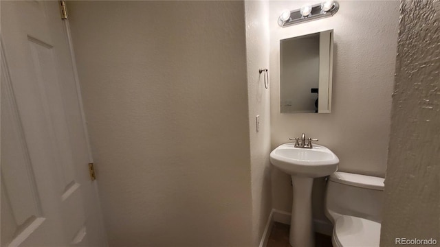 bathroom with a textured wall, a sink, and toilet