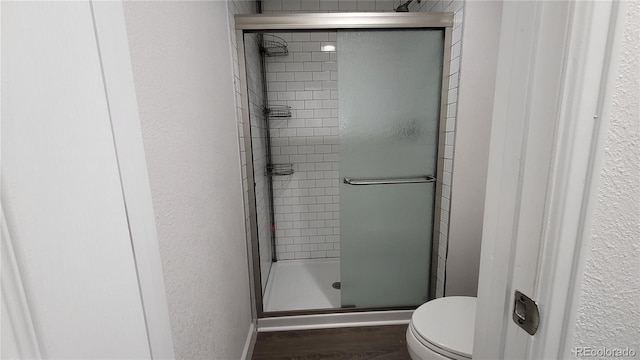 bathroom with a textured wall, a shower stall, toilet, and wood finished floors