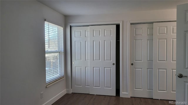 unfurnished bedroom with dark wood-style floors, baseboards, and multiple closets