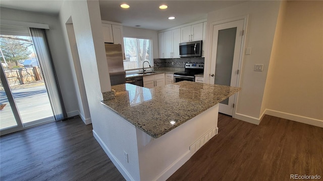 kitchen with light stone counters, appliances with stainless steel finishes, white cabinetry, a sink, and a peninsula