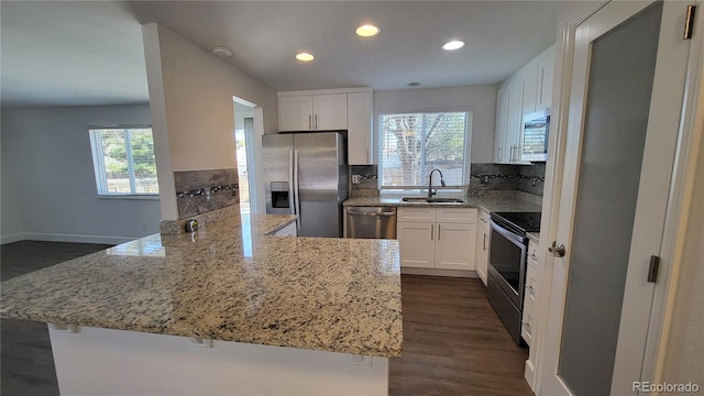 kitchen with light stone counters, a peninsula, a sink, white cabinets, and appliances with stainless steel finishes