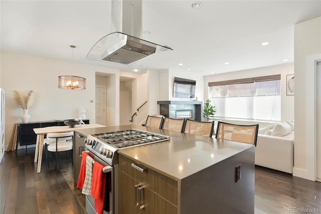 kitchen with stainless steel gas range, island range hood, hanging light fixtures, dark hardwood / wood-style floors, and a kitchen island