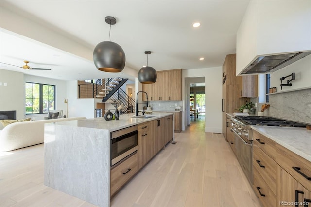 kitchen with pendant lighting, sink, custom exhaust hood, stainless steel appliances, and a center island with sink