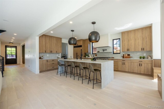 kitchen featuring hanging light fixtures, tasteful backsplash, a kitchen island with sink, light wood-type flooring, and a breakfast bar