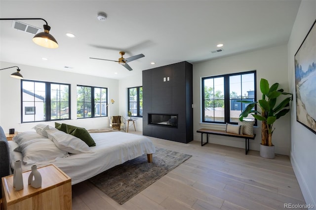 bedroom featuring ceiling fan, light hardwood / wood-style floors, a fireplace, and multiple windows