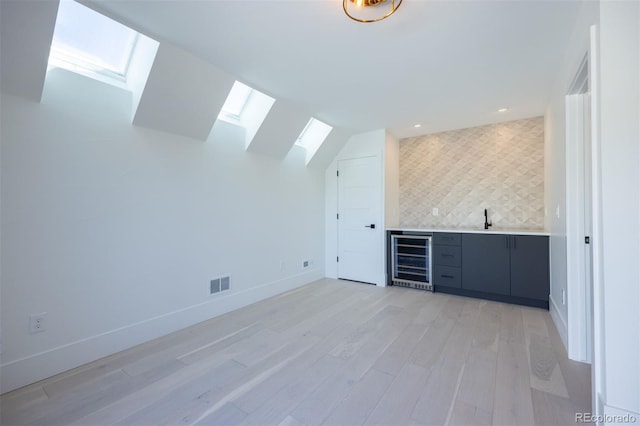 interior space with beverage cooler, light hardwood / wood-style flooring, vaulted ceiling with skylight, tasteful backsplash, and sink