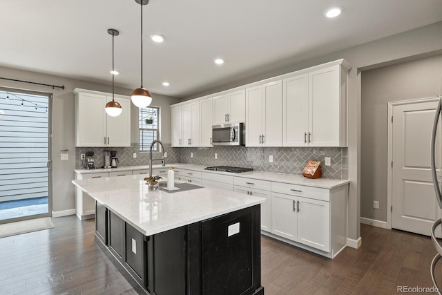 5841 Alton St, Denver, CO 80238 - kitchen featuring appliances with stainless steel finishes, dark wood finished floors, decorative backsplash, white cabinetry, and an island with sink