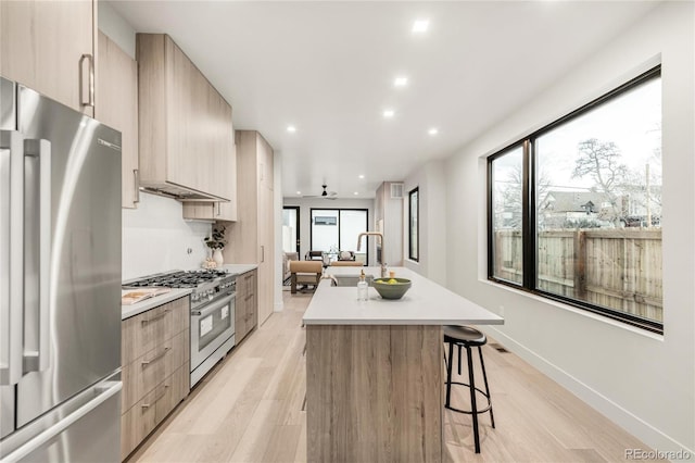 kitchen featuring sink, high end appliances, light wood-type flooring, a kitchen breakfast bar, and an island with sink