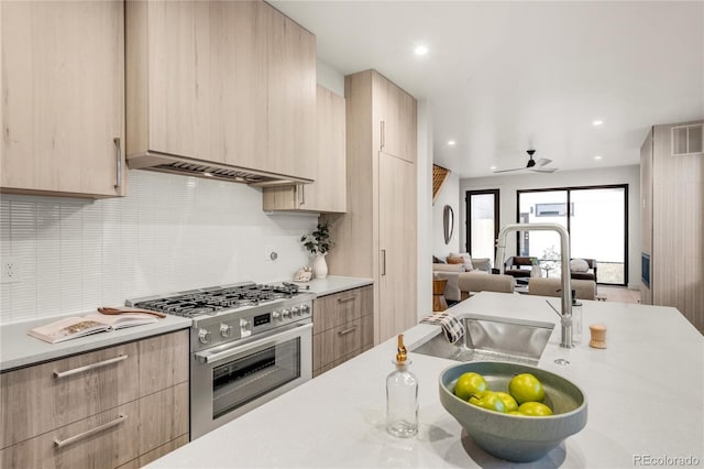 kitchen with stainless steel gas stove, tasteful backsplash, sink, ceiling fan, and light brown cabinets