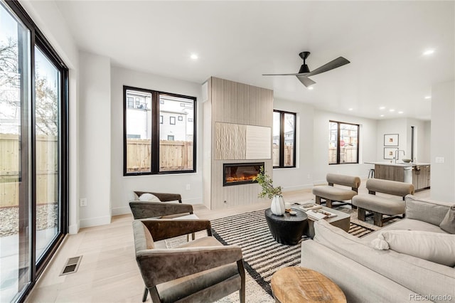 living room with a large fireplace, ceiling fan, and light wood-type flooring