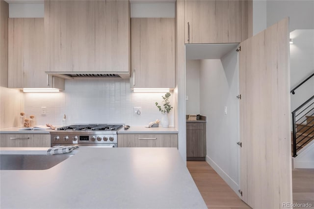 kitchen featuring light brown cabinetry, decorative backsplash, and stove