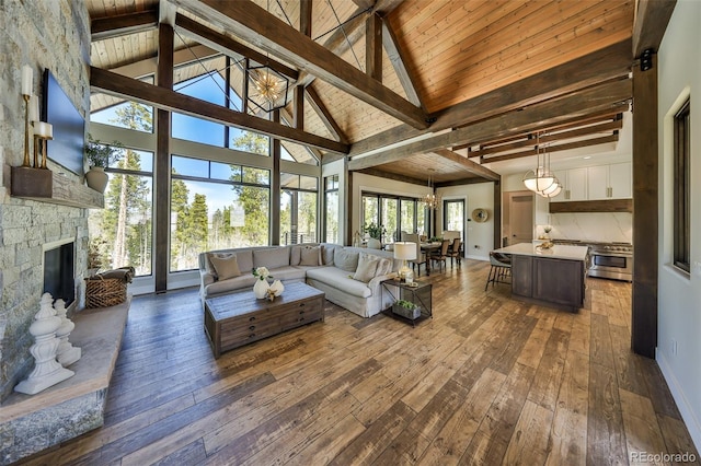 living area with beam ceiling, dark wood-type flooring, a stone fireplace, high vaulted ceiling, and a chandelier