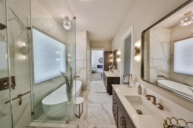full bath featuring marble tiled flooring, a freestanding tub, two vanities, and a marble finish shower