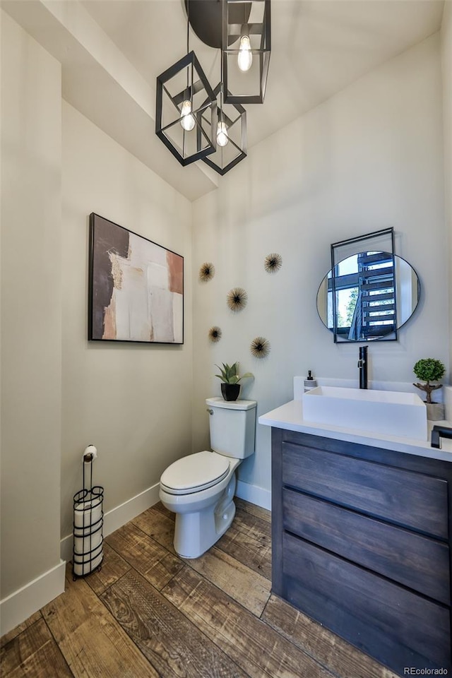half bath featuring toilet, wood finished floors, vanity, baseboards, and a chandelier