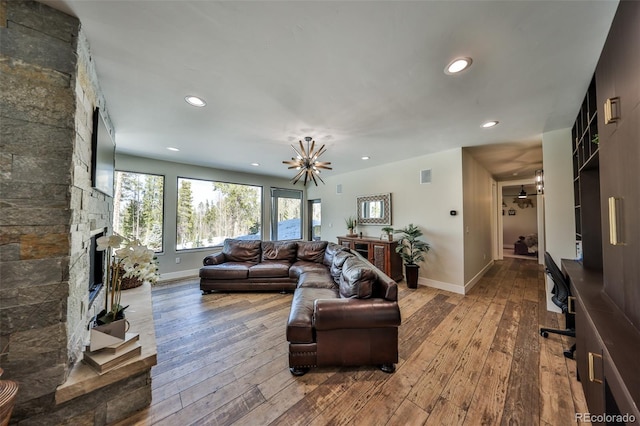 living area featuring wood-type flooring, a stone fireplace, recessed lighting, baseboards, and a chandelier