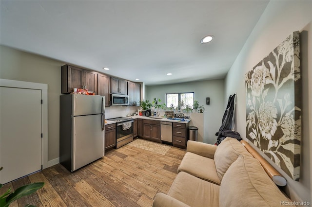 kitchen featuring appliances with stainless steel finishes, dark brown cabinetry, open floor plan, light wood-style flooring, and light countertops