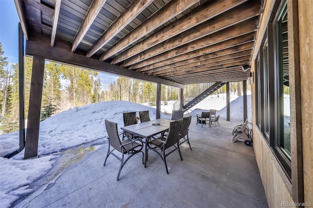 snow covered patio featuring outdoor dining space and stairs