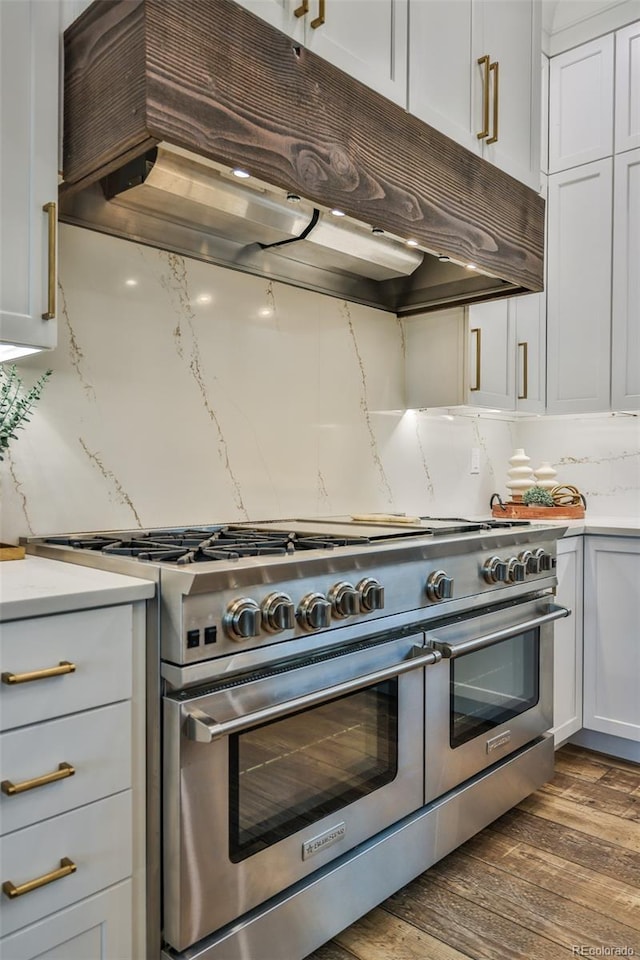 kitchen with extractor fan, range with two ovens, tasteful backsplash, dark wood-style flooring, and white cabinetry