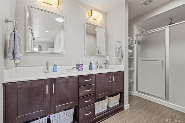 bathroom with double vanity, visible vents, a shower stall, and a sink