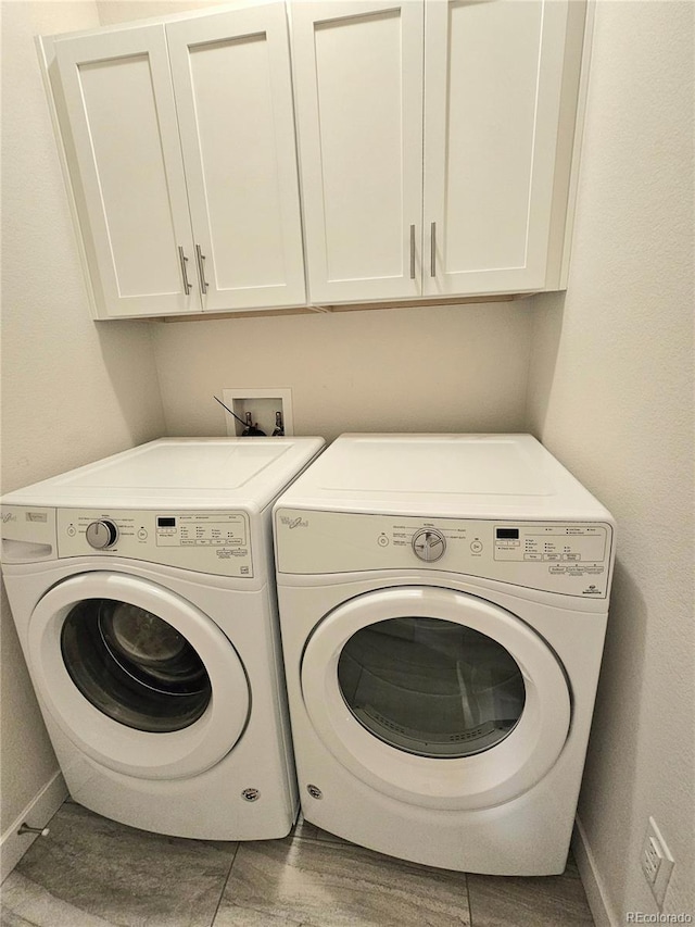 clothes washing area featuring washing machine and clothes dryer, tile patterned floors, and cabinets