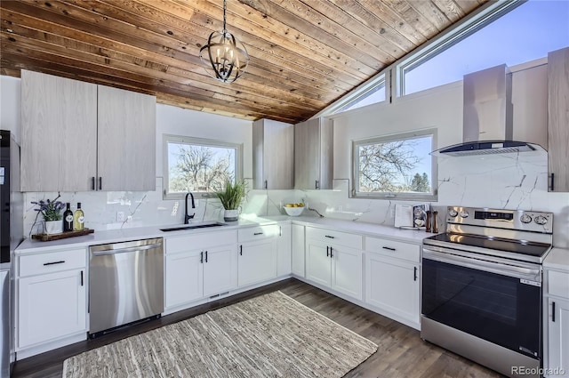 kitchen featuring wall chimney exhaust hood, sink, hanging light fixtures, appliances with stainless steel finishes, and white cabinets