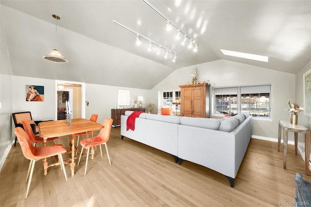 living room featuring vaulted ceiling with skylight, light wood-type flooring, rail lighting, and baseboards