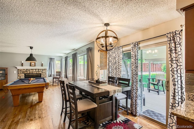 12013 W 56th Cir, Arvada, CO 80002 - dining area with light wood-type flooring, a textured ceiling, a stone fireplace, a chandelier, and billiards table