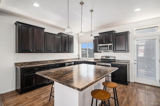 5048 N Andes St, Denver, CO 80249 - kitchen with appliances with stainless steel finishes, a kitchen bar, dark countertops, dark wood-style floors, and recessed lighting