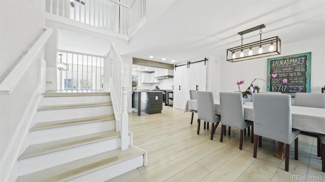 dining space featuring light wood finished floors, recessed lighting, a barn door, and stairway