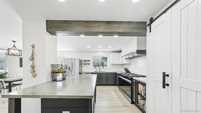 kitchen with a barn door, appliances with stainless steel finishes, beamed ceiling, light wood finished floors, and decorative backsplash