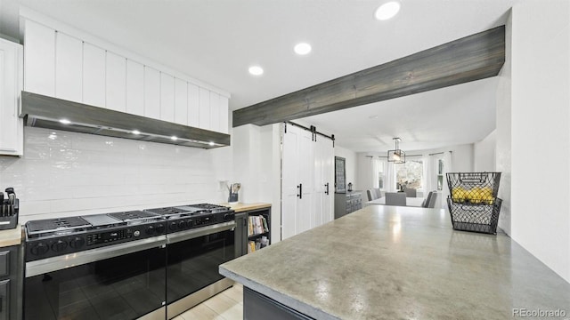 kitchen with white cabinets, tasteful backsplash, a barn door, and range with gas stovetop