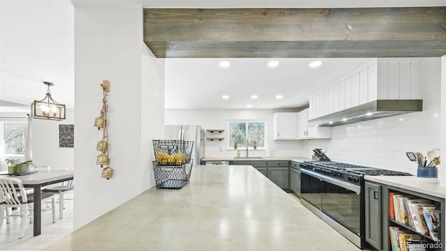 kitchen featuring a sink, wall chimney range hood, freestanding refrigerator, stainless steel gas range oven, and decorative backsplash