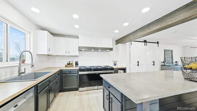 kitchen featuring range with gas stovetop, backsplash, a barn door, dishwasher, and a sink