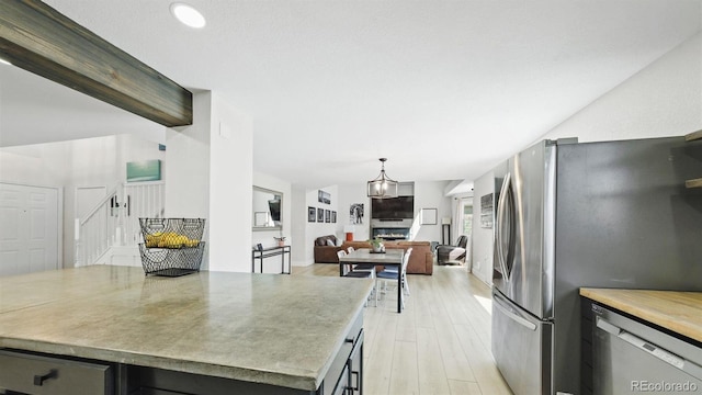 kitchen featuring hanging light fixtures, open floor plan, light countertops, appliances with stainless steel finishes, and light wood-style floors
