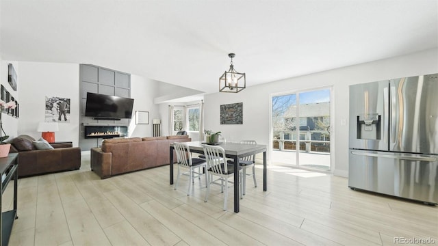 dining space featuring light wood finished floors, a notable chandelier, a large fireplace, and baseboards