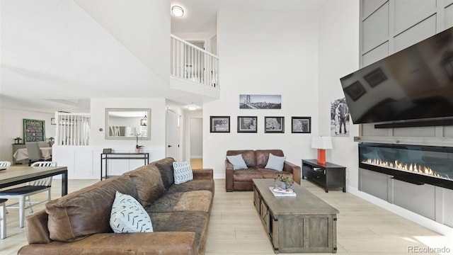 living room with a glass covered fireplace, a towering ceiling, light wood-style floors, and baseboards