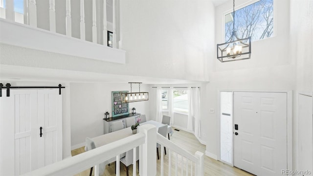 foyer featuring a barn door, light wood-style floors, a high ceiling, and an inviting chandelier