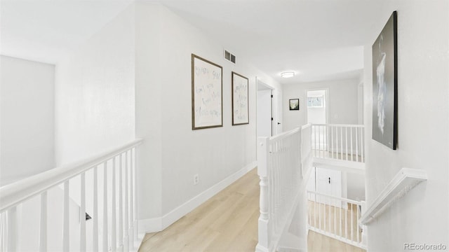 corridor featuring wood finished floors, visible vents, baseboards, and an upstairs landing