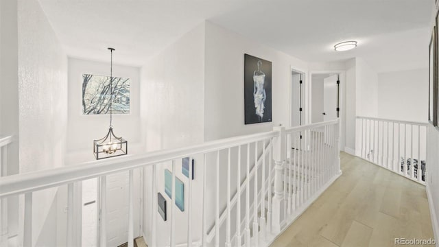 corridor with light wood-type flooring, an inviting chandelier, and an upstairs landing