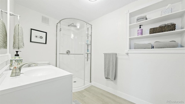 full bathroom with vanity, baseboards, a stall shower, visible vents, and wood finished floors