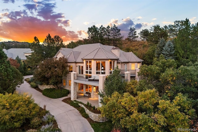 back of property featuring a balcony, stone siding, a tiled roof, a patio area, and stucco siding