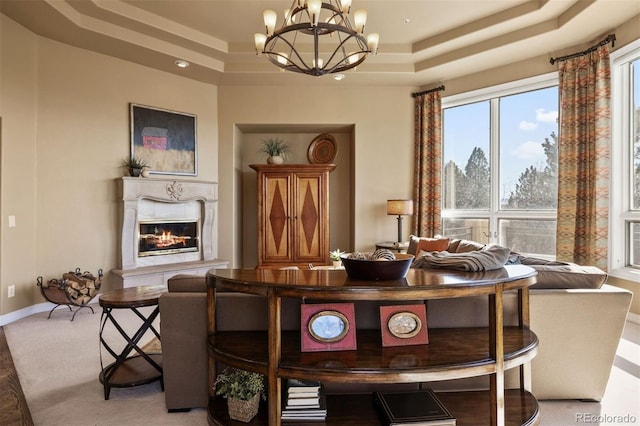 dining room featuring a tray ceiling, a premium fireplace, light carpet, a chandelier, and baseboards