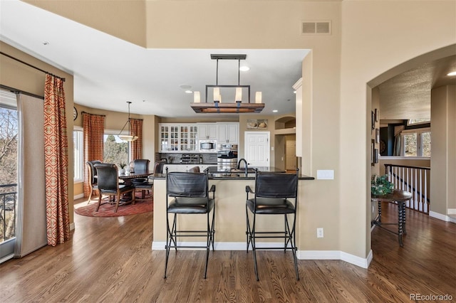 kitchen with glass insert cabinets, dark wood-style flooring, stainless steel microwave, and visible vents