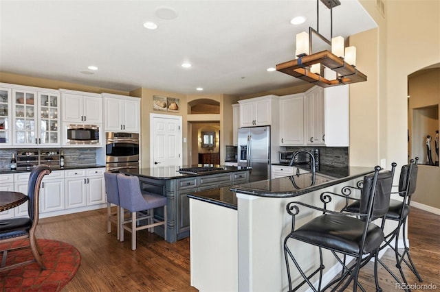 kitchen with arched walkways, appliances with stainless steel finishes, white cabinetry, and a kitchen breakfast bar