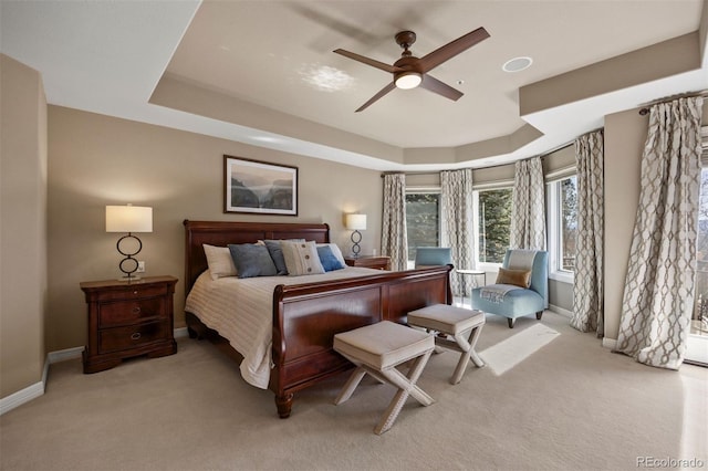 bedroom with light carpet, baseboards, a tray ceiling, and ceiling fan