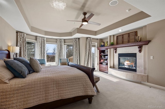 bedroom featuring access to exterior, a tray ceiling, carpet flooring, and a fireplace