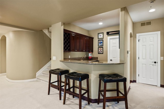 kitchen featuring arched walkways, visible vents, light carpet, and a breakfast bar area